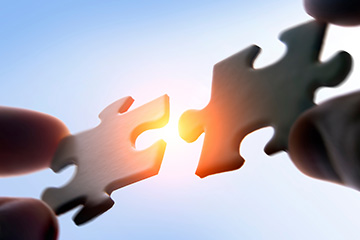 The image depicts two hands holding a puzzle piece together, symbolizing unity or collaboration.