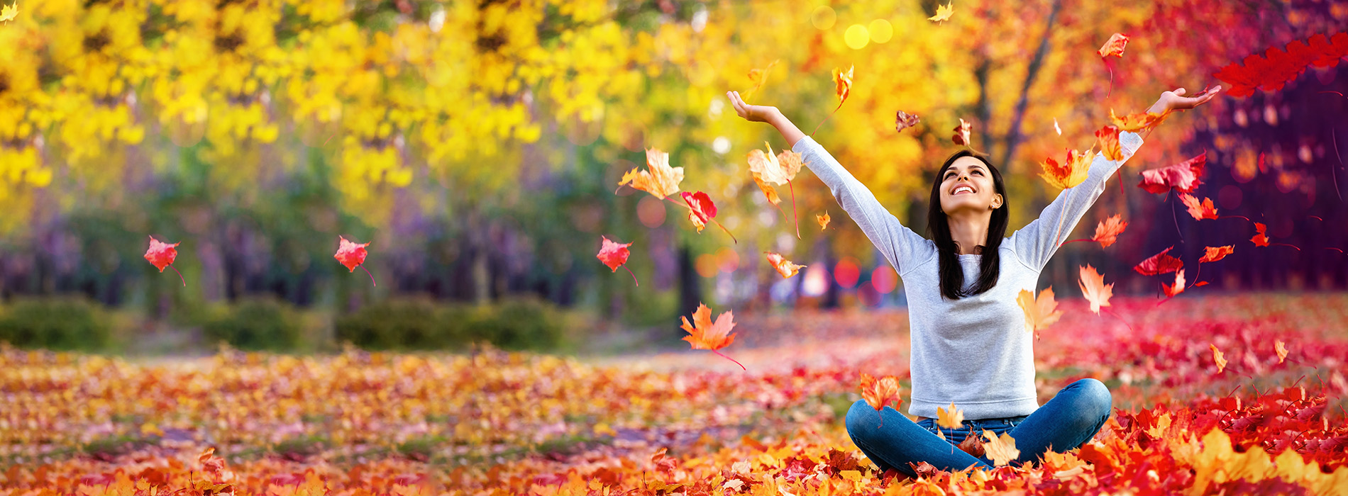 A person sitting on the ground amidst fallen autumn leaves, enjoying a moment of relaxation and happiness.